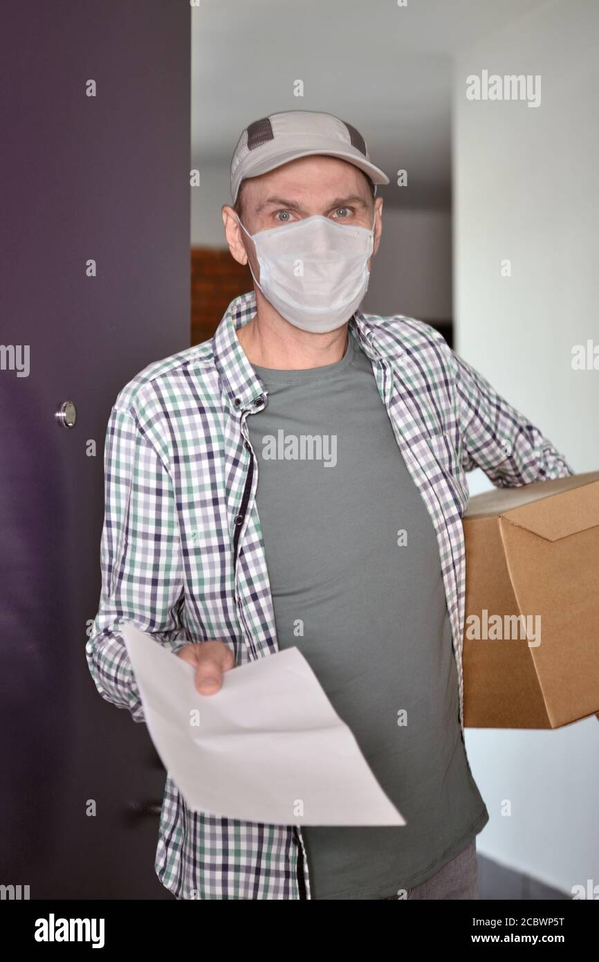 Delivery man in medical face mask with a box in the doors Stock Photo