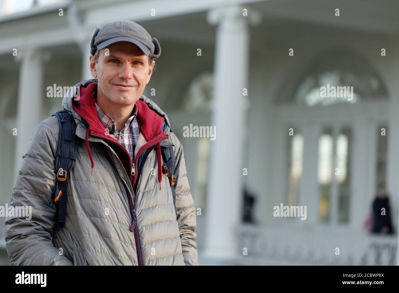 Smiling mature Caucasian man standing with backpack against a pavilion in a city garden Stock Photo