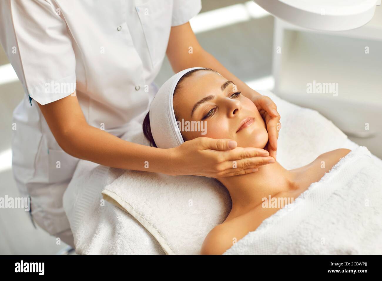 Hands of cosmetologist massaging relaxed womans face in spa beauty salon Stock Photo