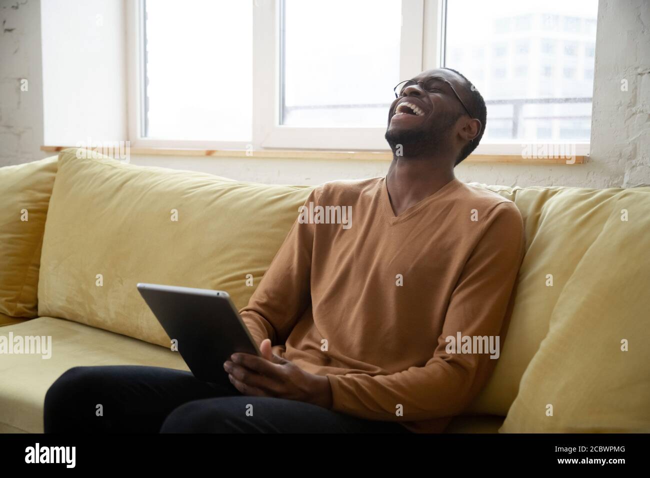 Cheerful black man laughing watching videos online on digital tablet Stock Photo