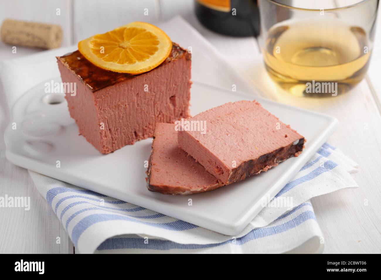 Sliced duck pate topped with slice of orange and a cup of white wine closeup Stock Photo