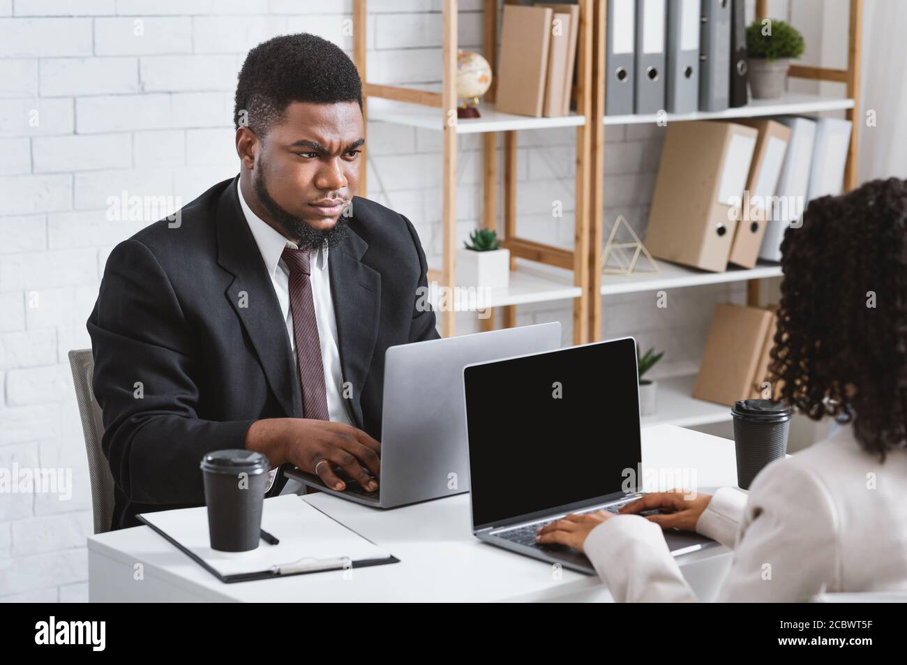Workplace conflict. Displeased African American guy having disagreement with his female colleague at office, free space Stock Photo