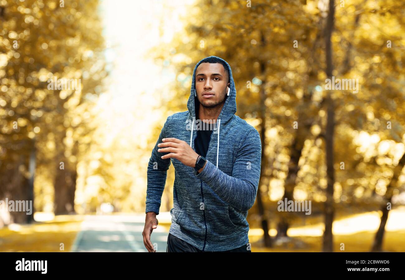 Handsome black sportsman in hoodie running outdoors on autumn day Stock Photo