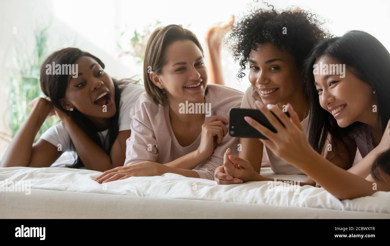 Multiracial girls enjoy time together lying in bed using smartphone Stock Photo