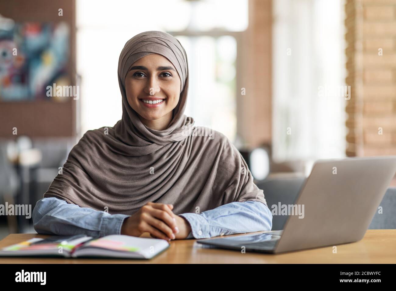 Smiling arab girl looking for job online, sitting at cafe Stock Photo