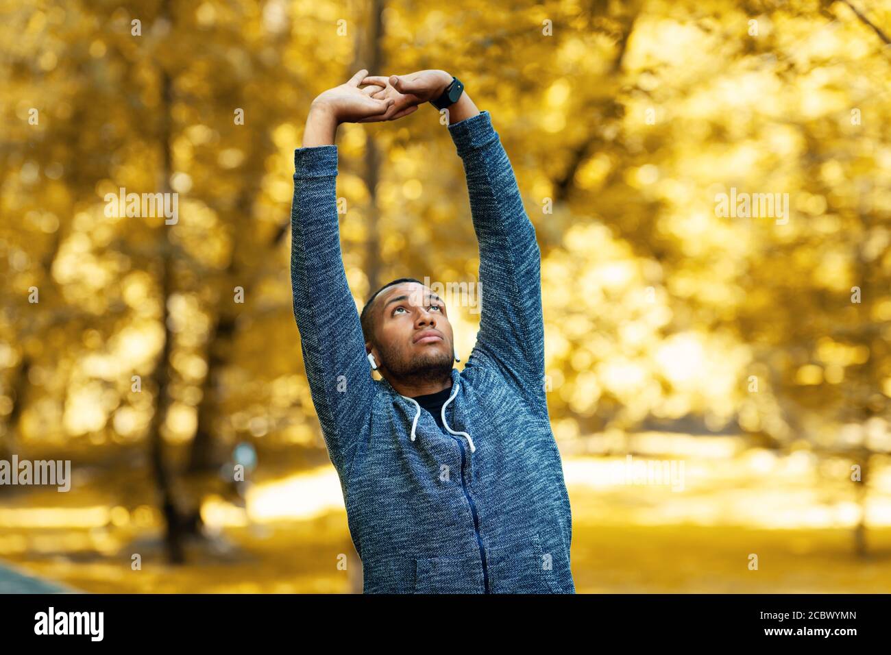 Millennial black sportsman stretching his arms before jogging at park on autumn morning Stock Photo