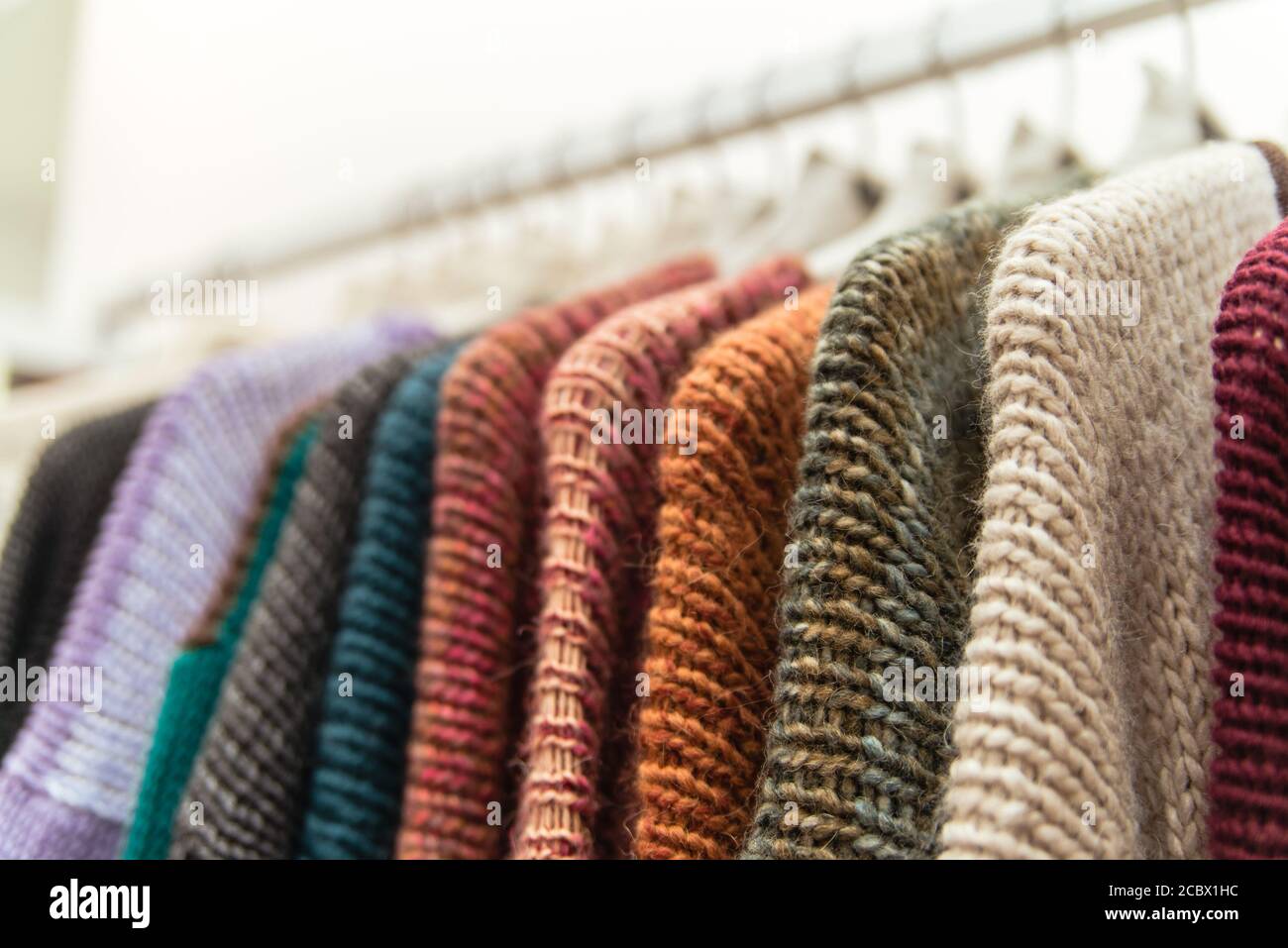 Nice warm colorful sweaters hang on hangers inside of a shopping mall. Beautiful clothes for winter autumn season. Wool things for fall. Classic Stock Photo