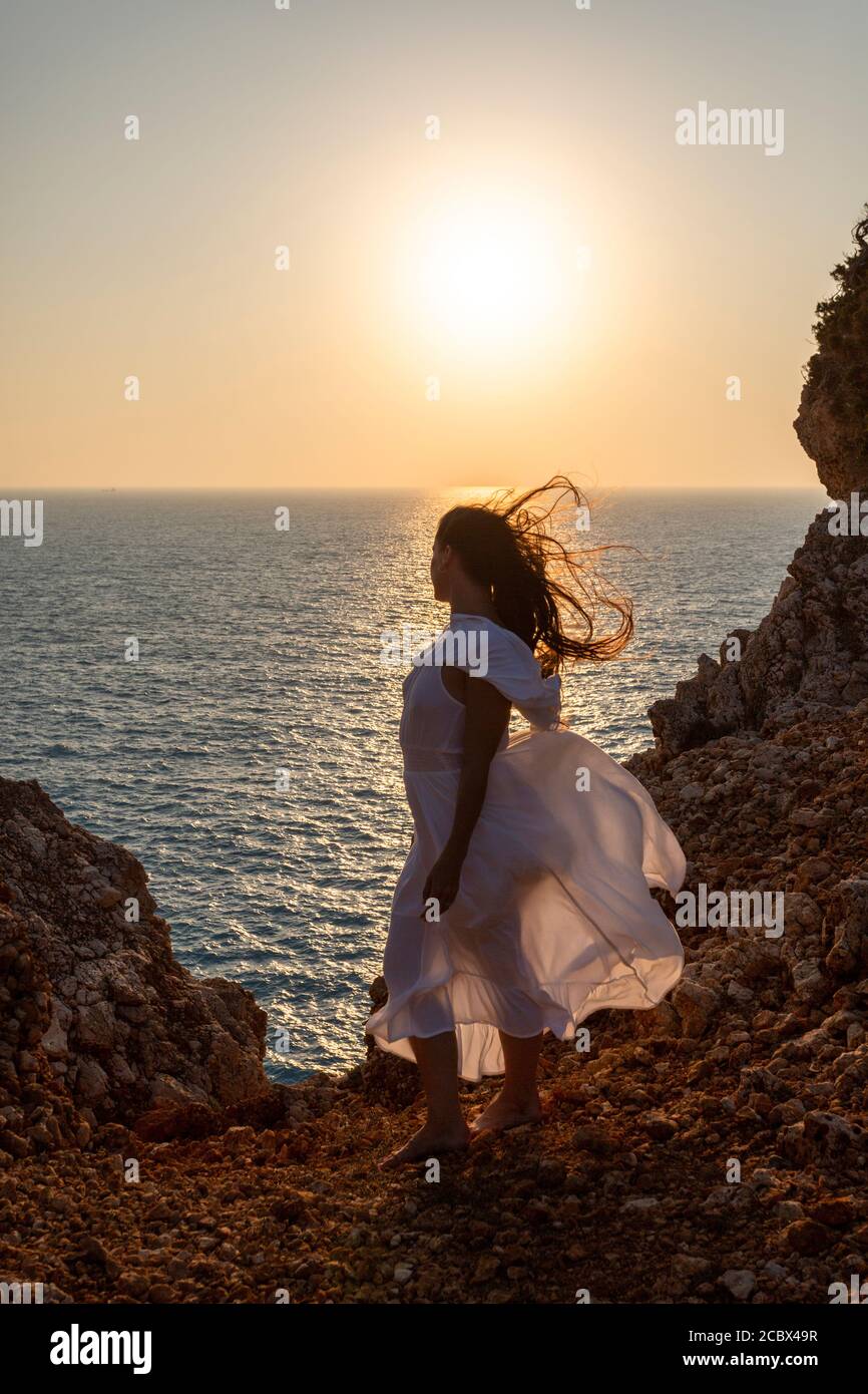 A girl in white dress on the windswept Cape Lefkada at sunset, Lefkada, Ionian Islands, Greece Stock Photo