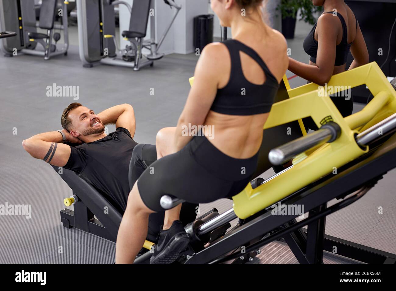 fit girls support sportsman whie he is doing exercises on equipment. male pumping legs, in