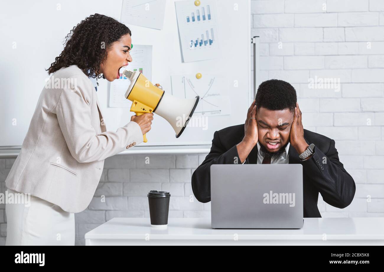 Angry African American lady boss with loudspeaker screaming at frightened male employee in office Stock Photo