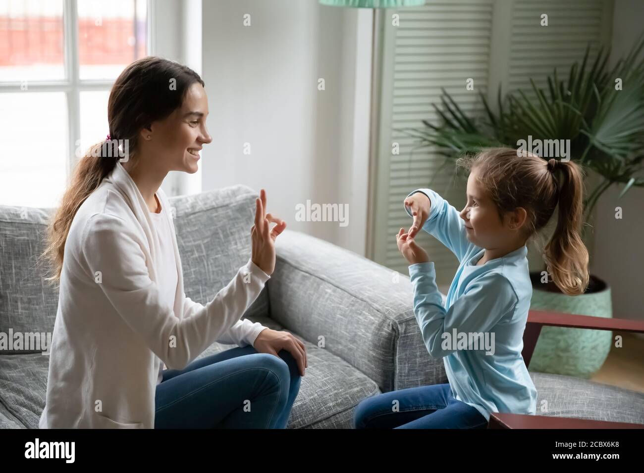 Smiling young woman teaching little cute girl sign language. Stock Photo