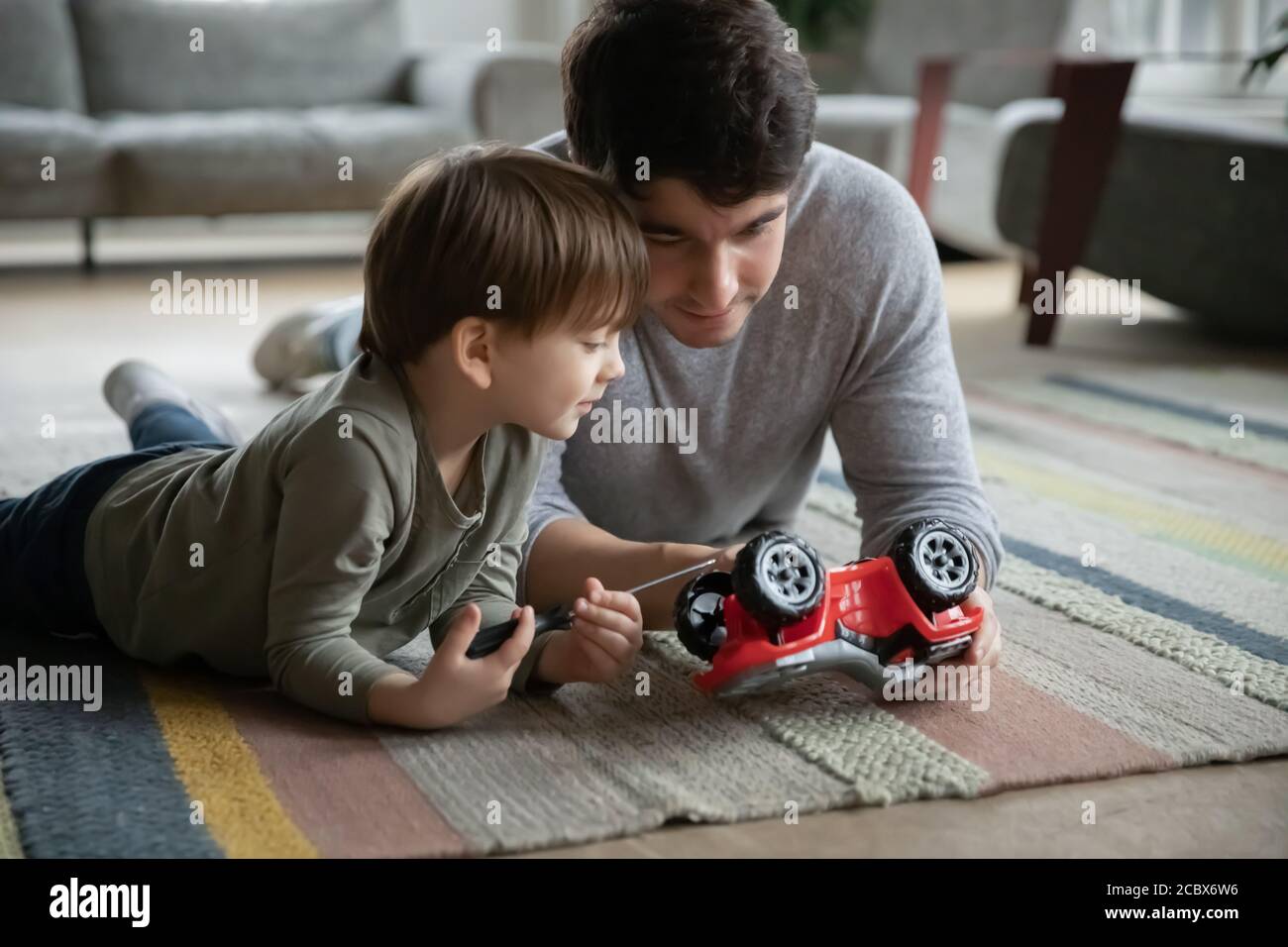 Caring young father fixing toy car with kid son. Stock Photo