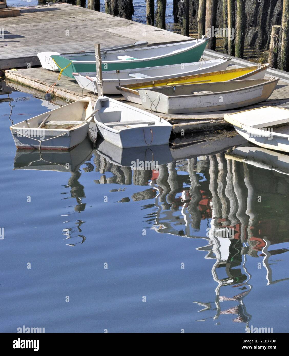 Late summer afternoon in coastal Maine. Undulating reflections of small boats and pier on rippling surface of water. Vertical image. Stock Photo