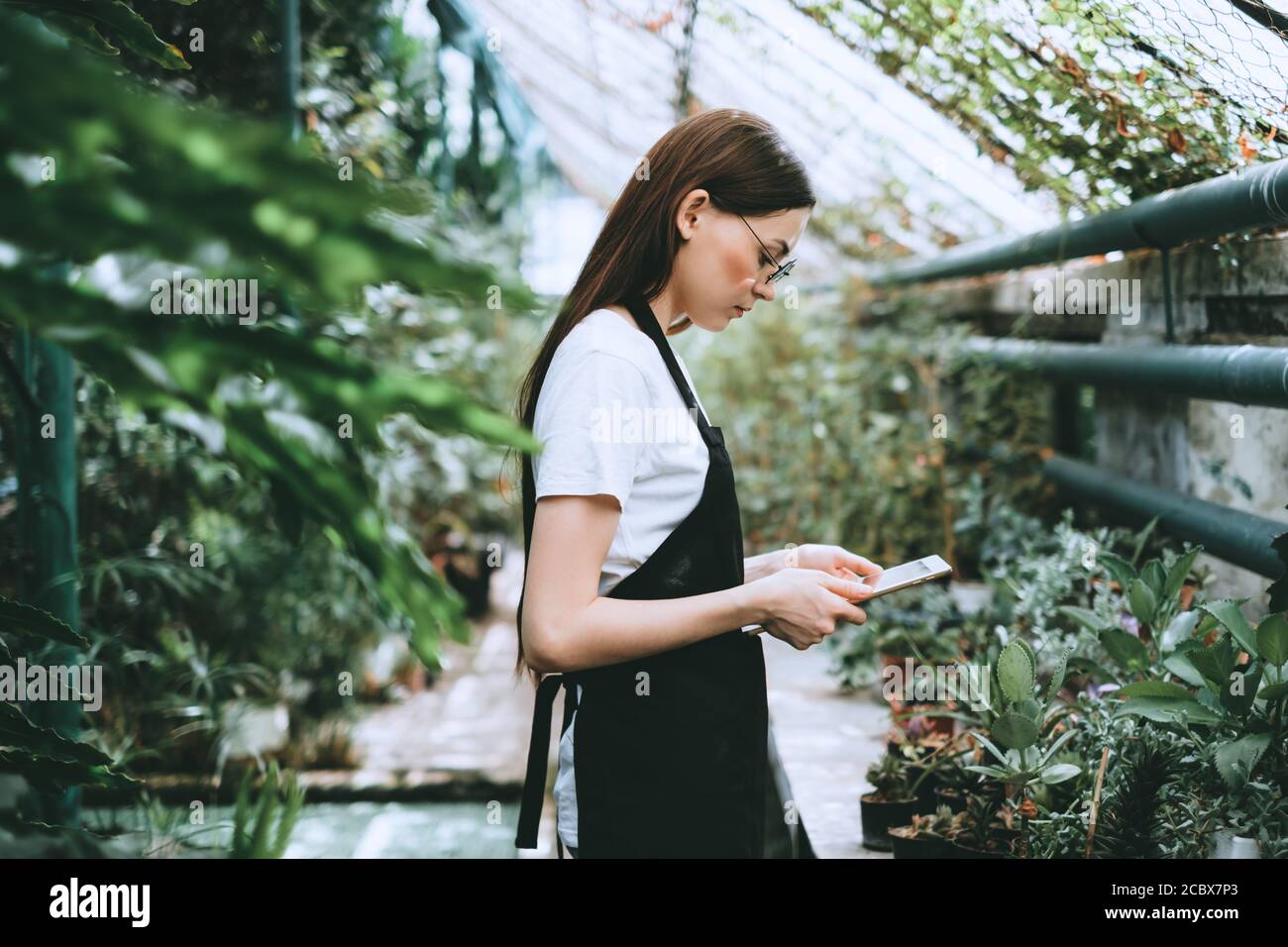 Young woman gardener in glasses with digital tablet working in a garden ...