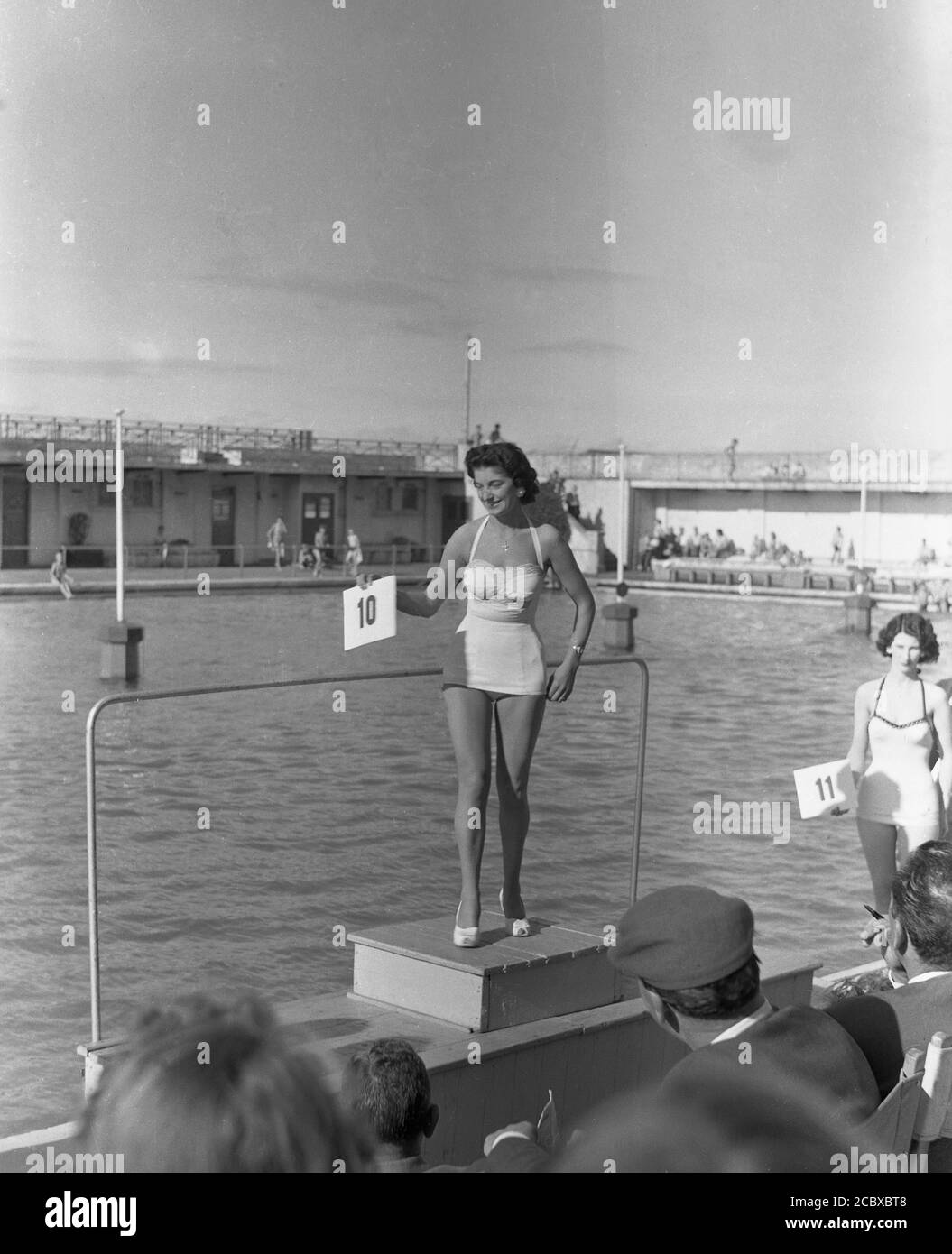 1960s, historical, a lady contestant in a bathing beauty contest standing on a platform beside an outdoor swimming pool showing her number to the audience, possibly at Morecambe. Beauty contests or pageants were a popular form of entertainment in the seaside towns of post-war Britain for the holiday-makers and providing cash prizes for those taking part. Stock Photo