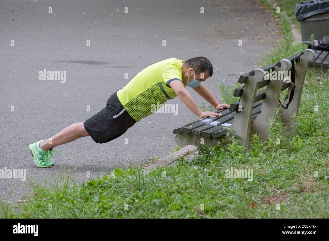 An Asian American man wearing a surgical mask does bench pushup exercises in a park in Flushing, Queens, New York City. Stock Photo
