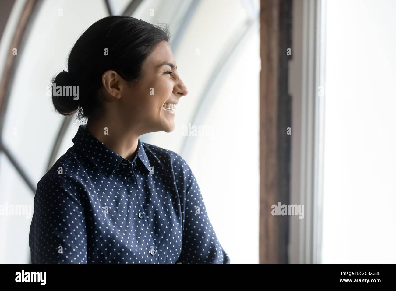 Overjoyed young emotional indian woman looking out of window. Stock Photo