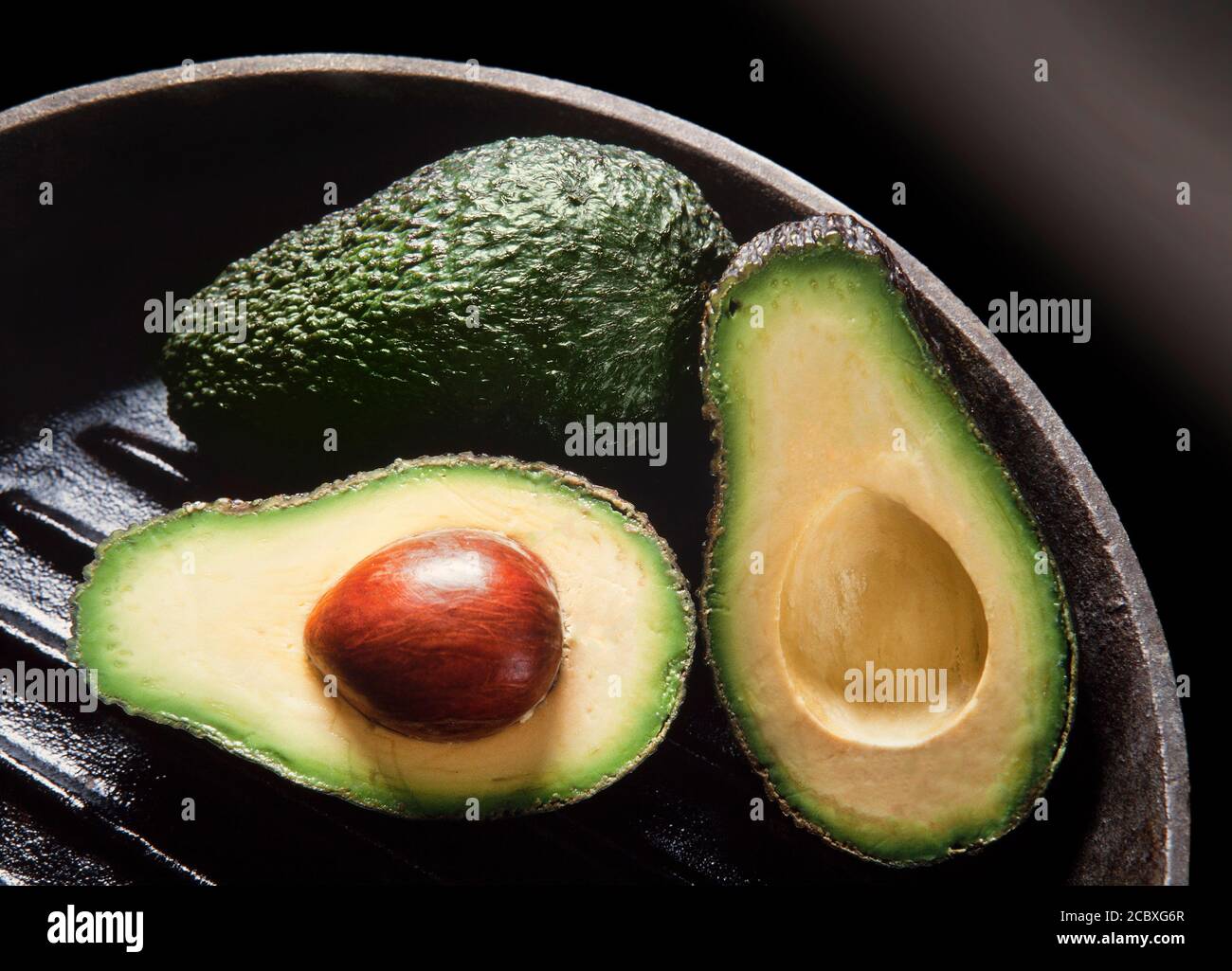 Avocado pear, Persea americana, split open showing flesh and large nut. Stock Photo