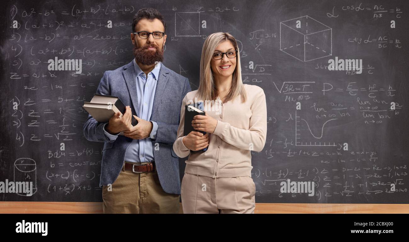 Male and female teacher holding books in front of a school blackboard Stock Photo