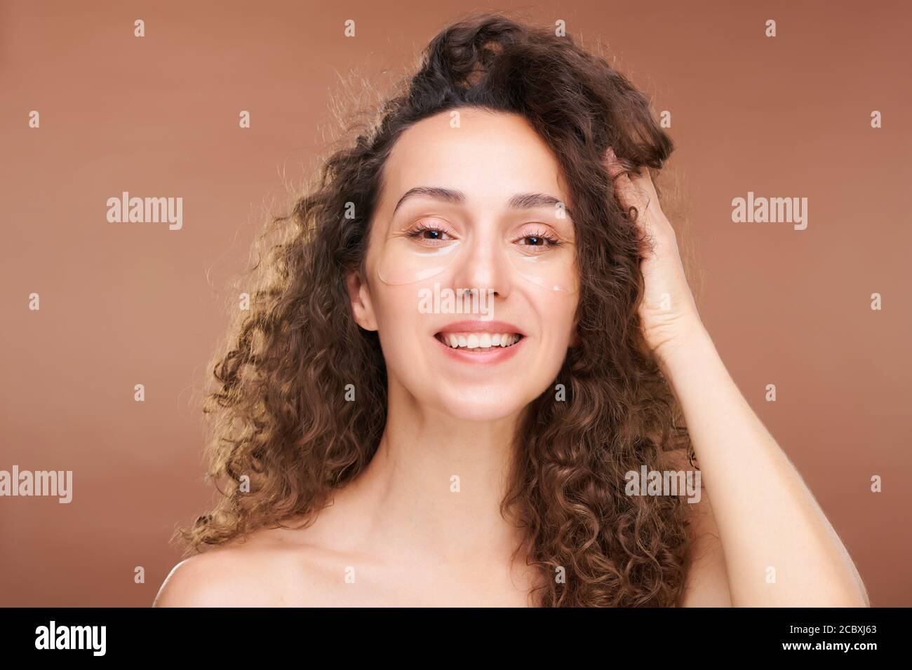 Young happy brunette woman with undereye patches touching long wavy hair Stock Photo
