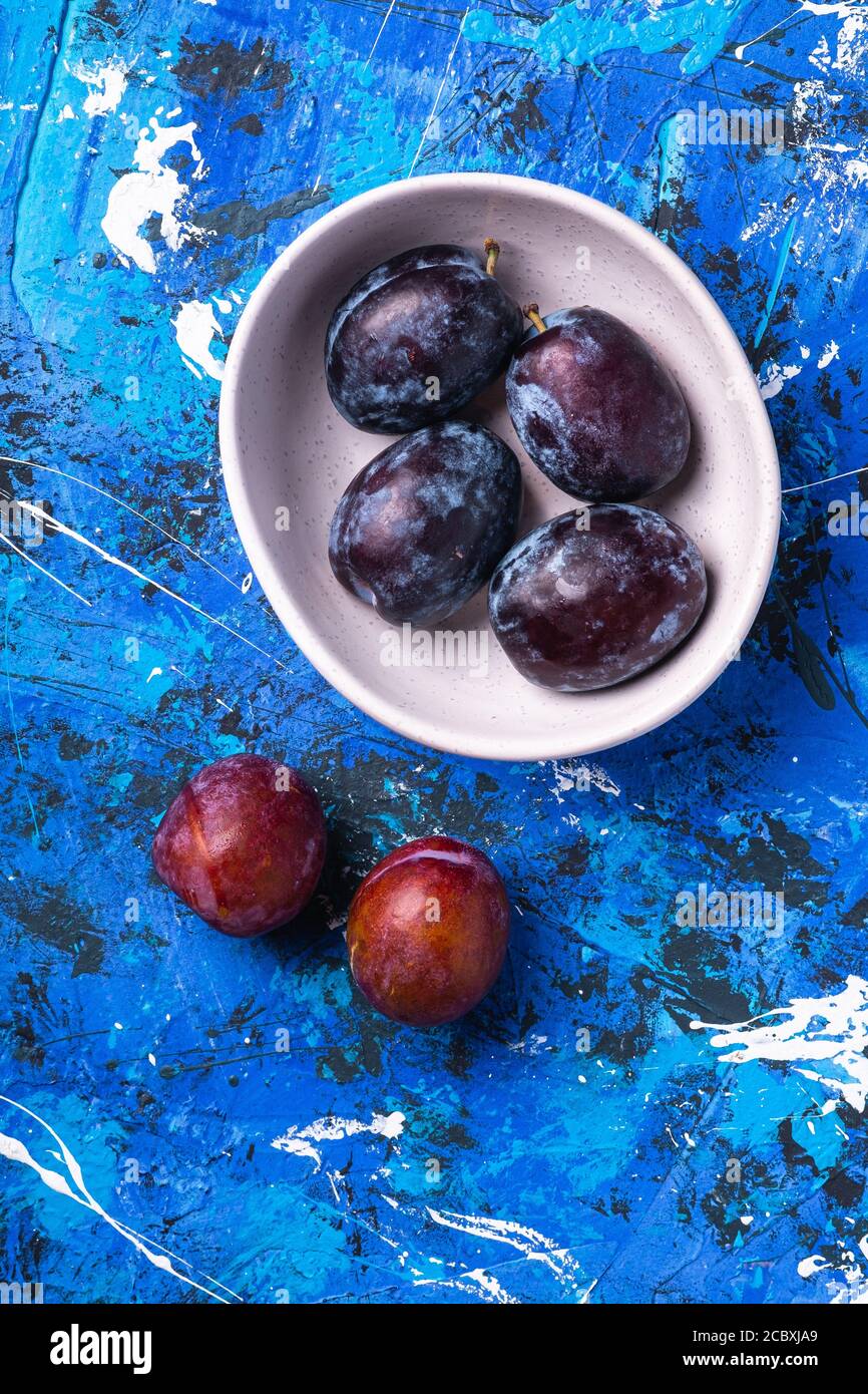 Fresh sweet plum fruits in white bowl on blue abstract background, top view Stock Photo Alamy