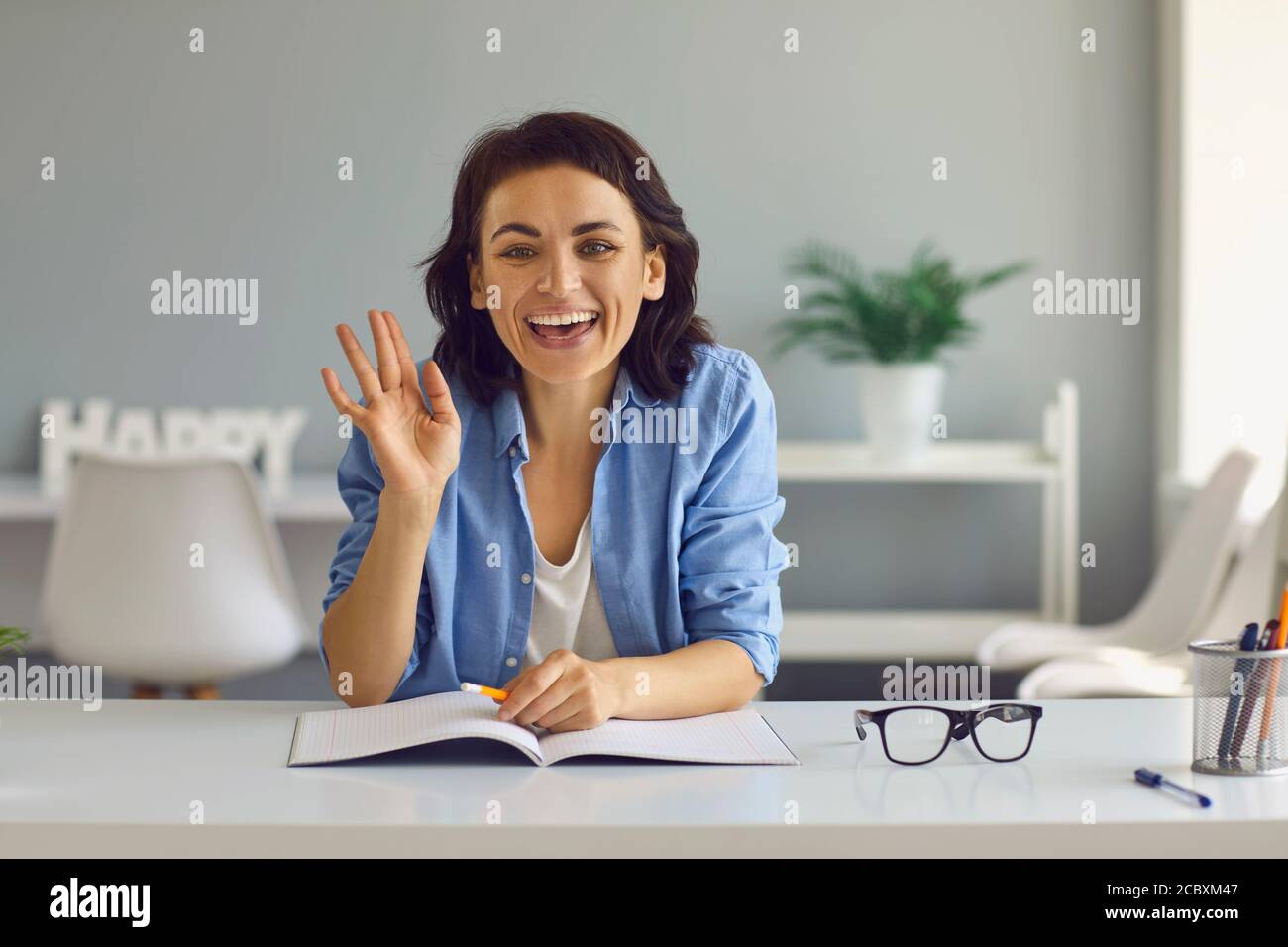 Young smiling woman looking at camera and greeting people online at home Stock Photo