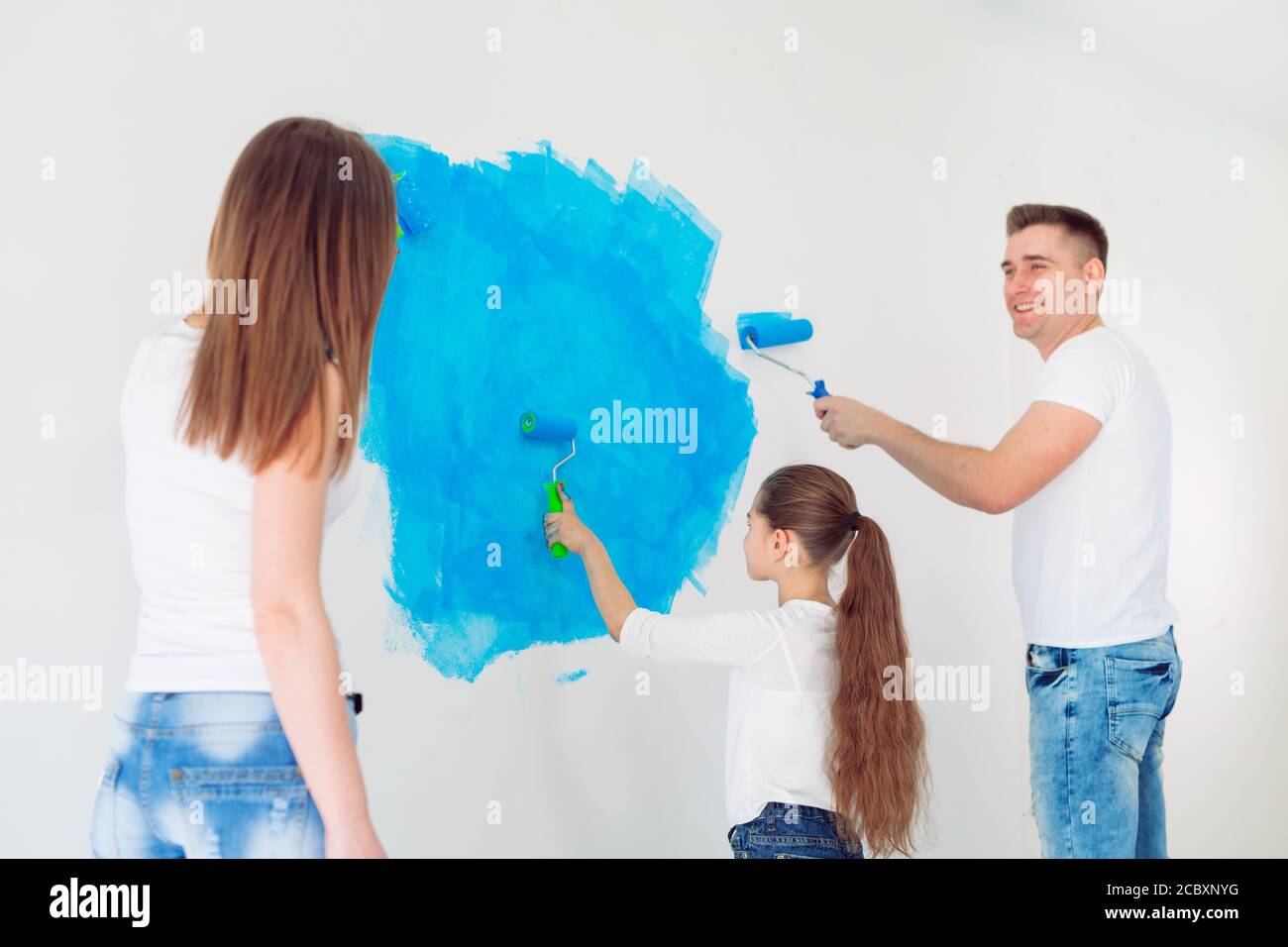 Mother, father and little daughter painting the wall in their new home ...