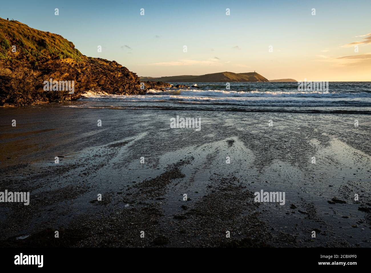 Early evening view of Polzeath beach with the rocks reflecting the setting sun and patterns from the retreating tide. Stock Photo