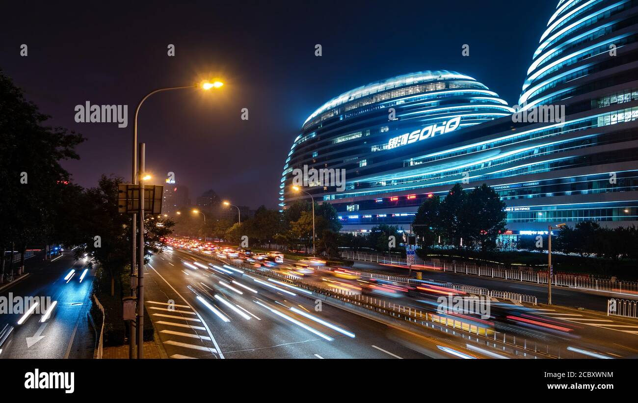 Night traffic on highway next to modern architectural landmark Galaxy SOHO urban complex in Beijing, China. Stock Photo