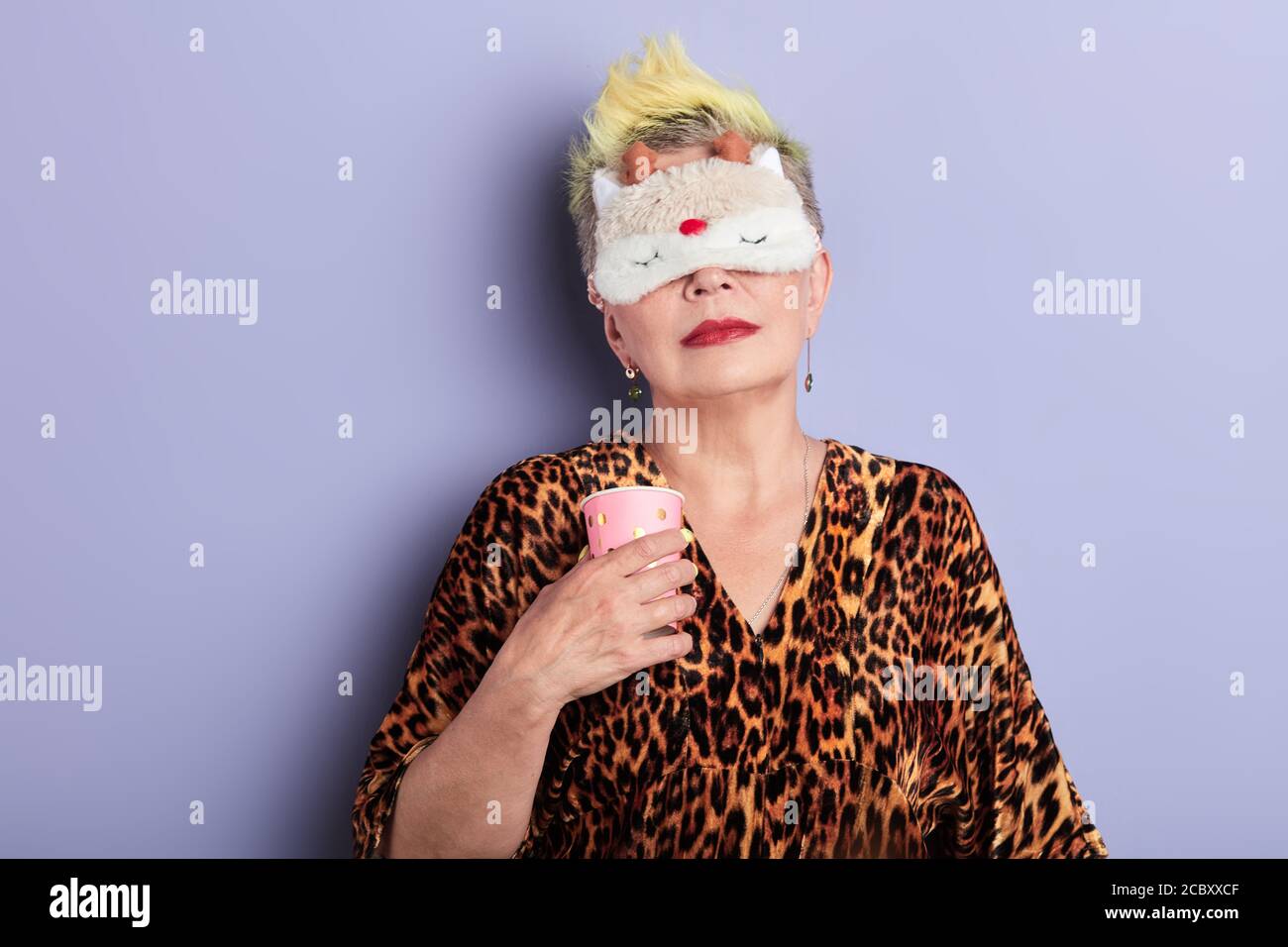 tired old woman doesn't want to go to work, serious mature woman in sleeping mask holding coffee in the morning, daily life. free time, coffee break Stock Photo