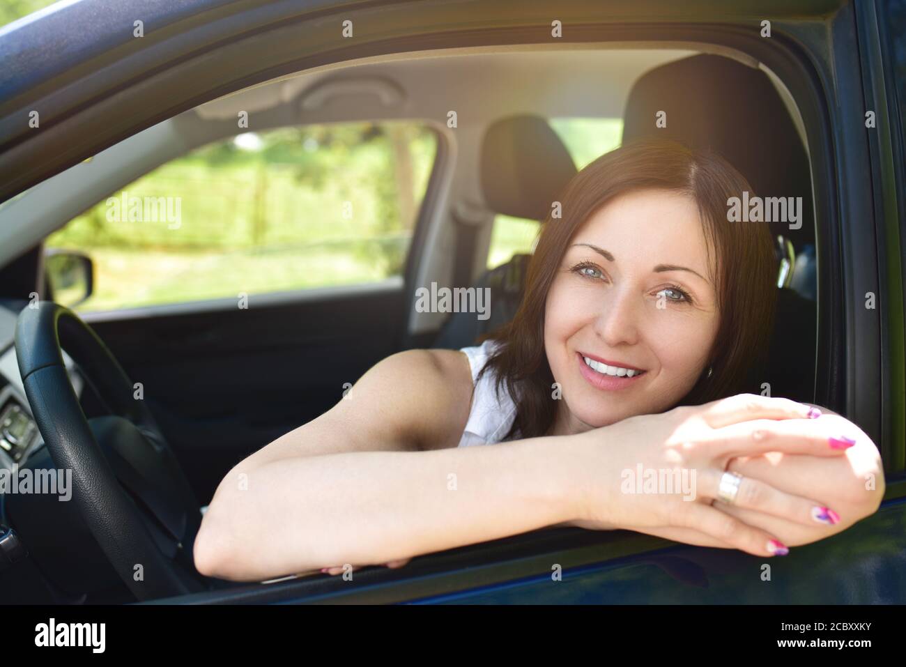 Smiling female driver looking out the car. a portrait of a smiling woman sitting in the car, looking at the camera. Stock Photo
