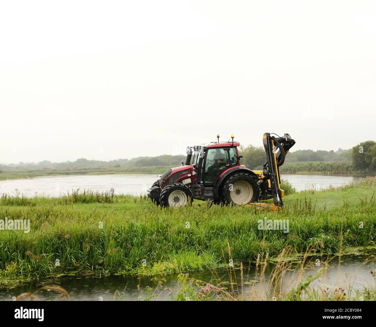 August 2020 - Environment Agency tractor mowing and grass cutting beside a river / drain Stock Photo