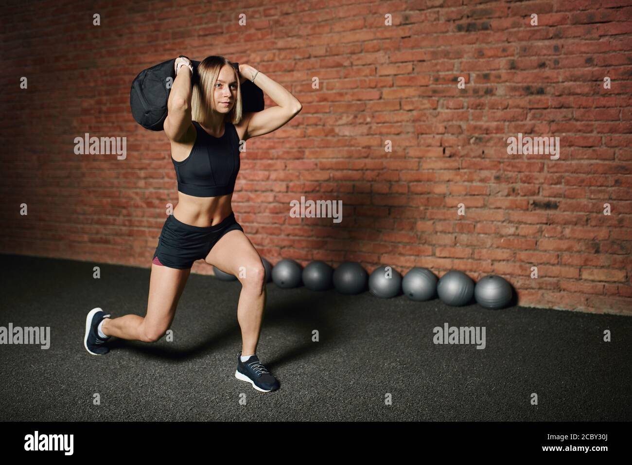 Young female athlete doing lunges with weight holding in hands heavy sandbag during circuit functional training at cross fit studio Stock Photo Alamy