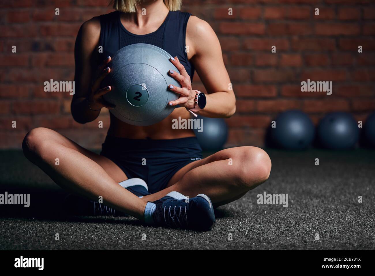 Fit well-trained woman in black sports wear posing with medicine ball during pilates workout in fitness centre. Stock Photo