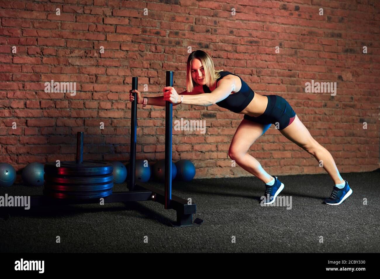 Fulllength side view of young athletic woman doing sled training