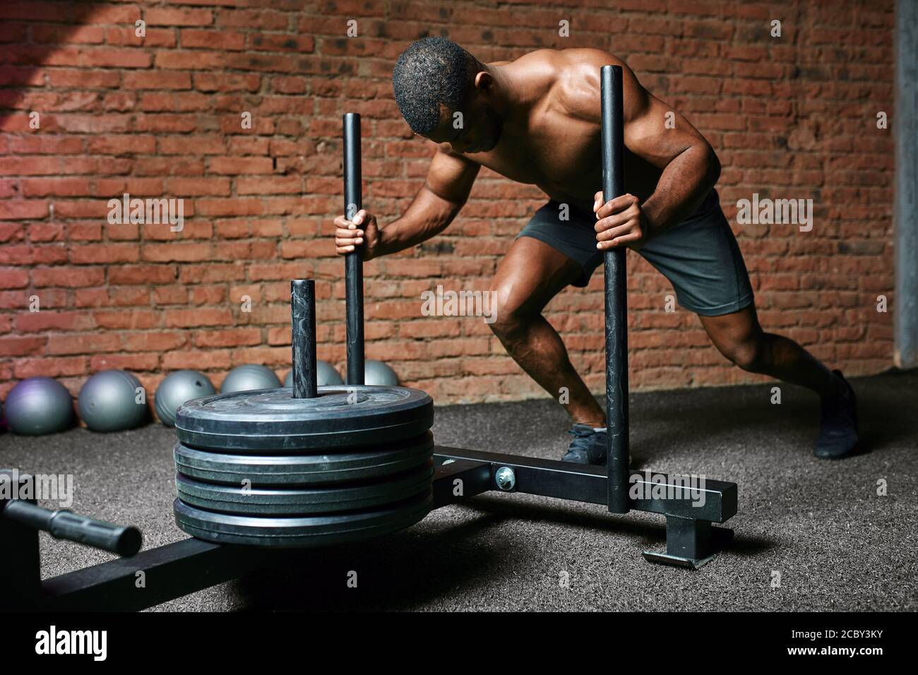 Darkskinned male bodybuilder performing heavy weight Sled Push