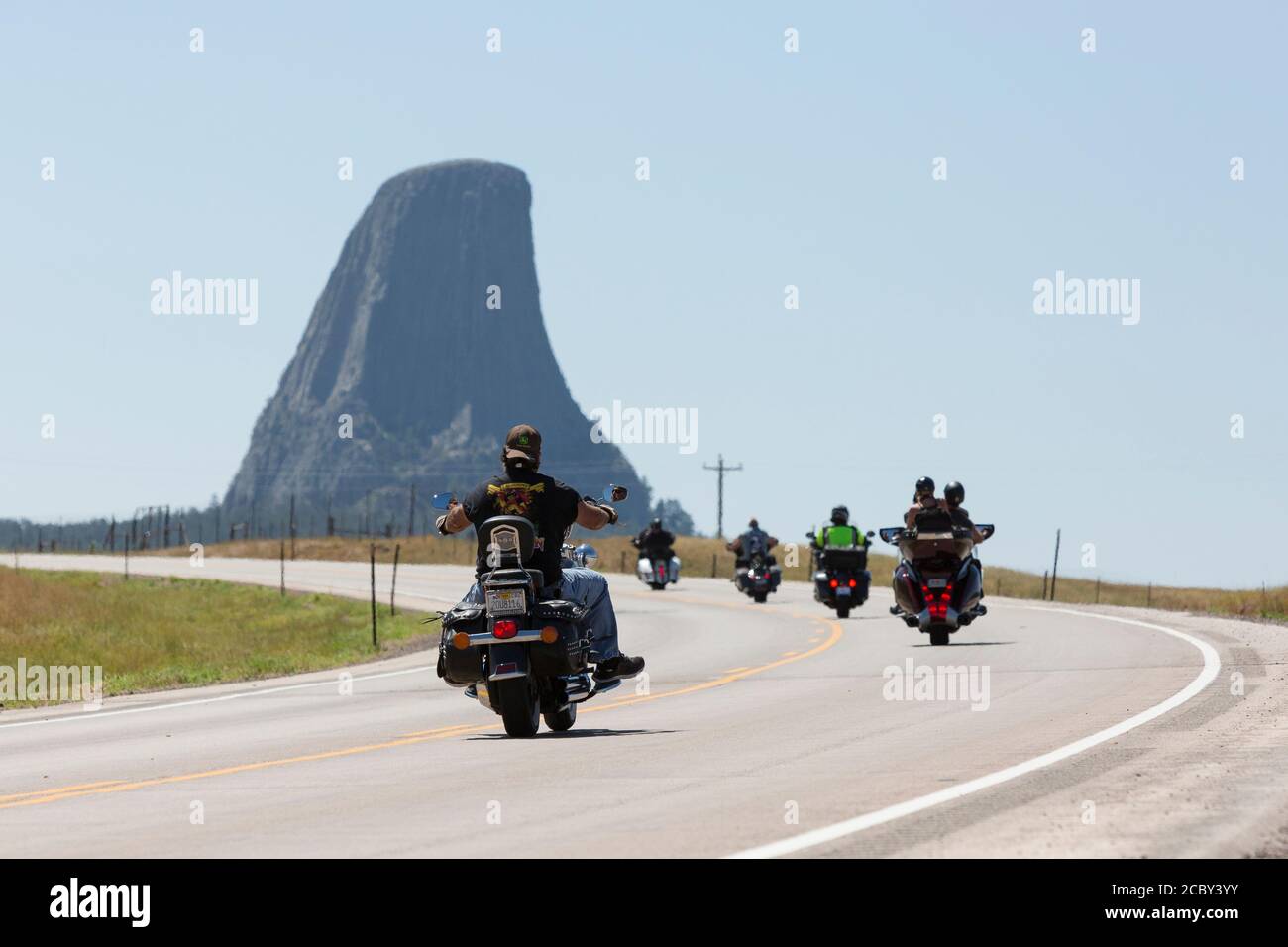 Bikers cruise along Highway 24 near Wyoming’s Devils Tower on Friday, August 14, 2020. Every year, bikers who attend the nearby Sturgis Motorcycle Rally in South Dakota descend on the iconic landmark. Stock Photo