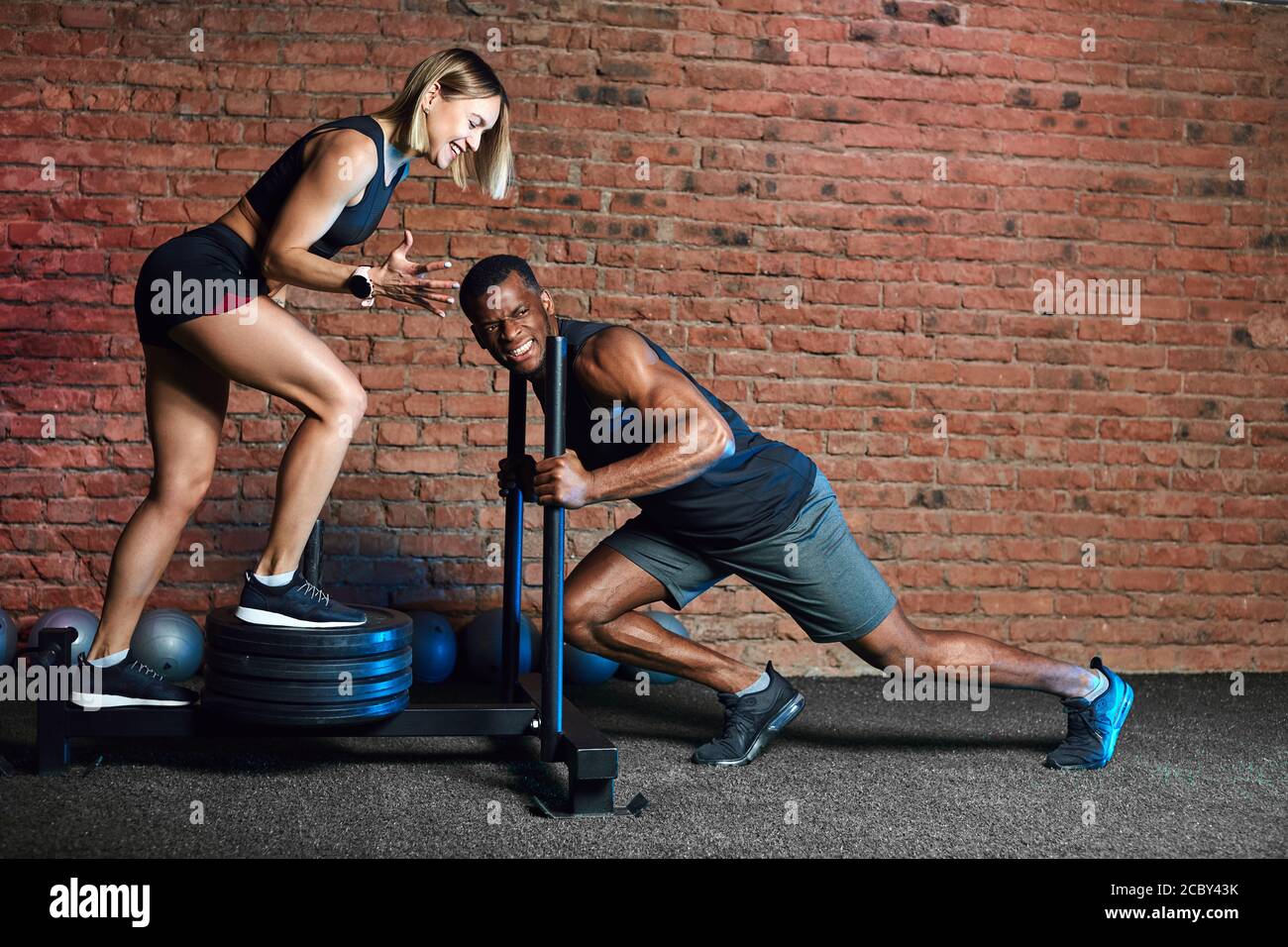 African athlete working out with heavy weight Sled Push machine and blonde  european woman supports him at indoor cross fit studio Stock Photo - Alamy