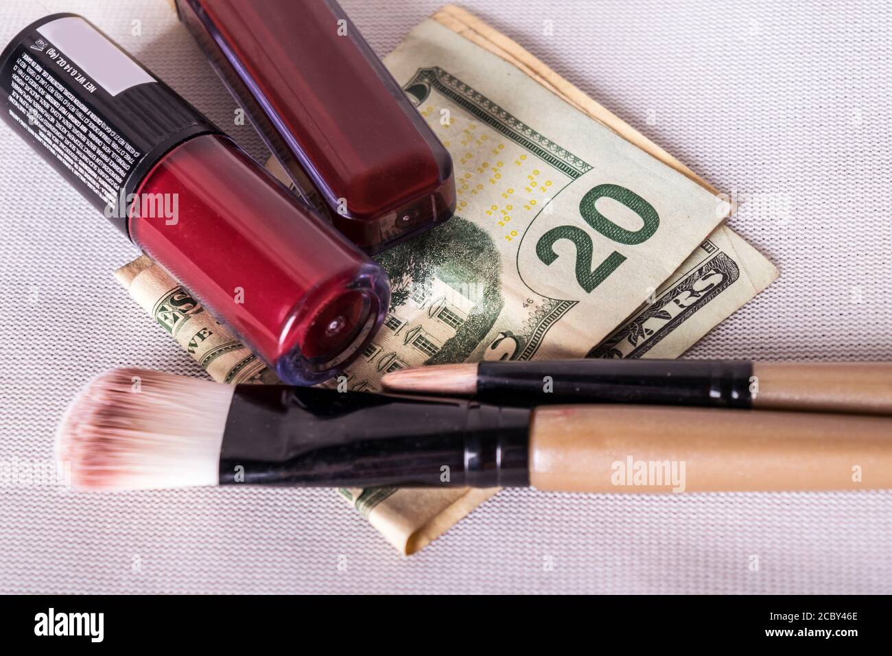 A flat lay photo of red lipsticks and make up brushes all on top of folded dollar bills Stock Photo
