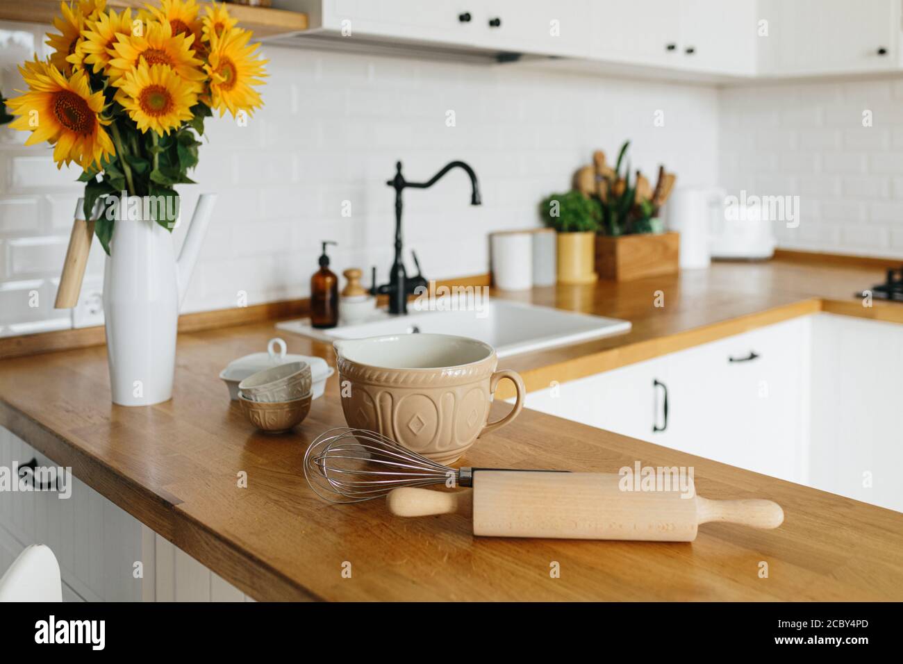 https://c8.alamy.com/comp/2CBY4PD/dishes-and-utensils-on-kitchen-table-ready-to-cook-white-simple-modern-kitchen-in-scandinavian-style-kitchen-details-wooden-table-sunflowers-bouq-2CBY4PD.jpg