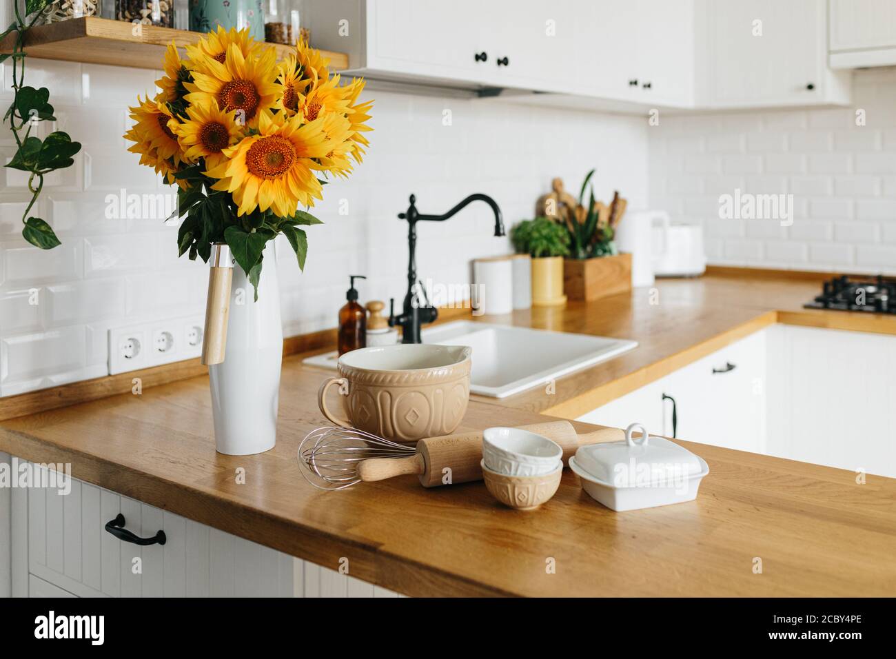 Dishes and utensils on kitchen table, ready to cook. white simple modern kitchen in scandinavian style, kitchen details, wooden table, sunflowers bouq Stock Photo