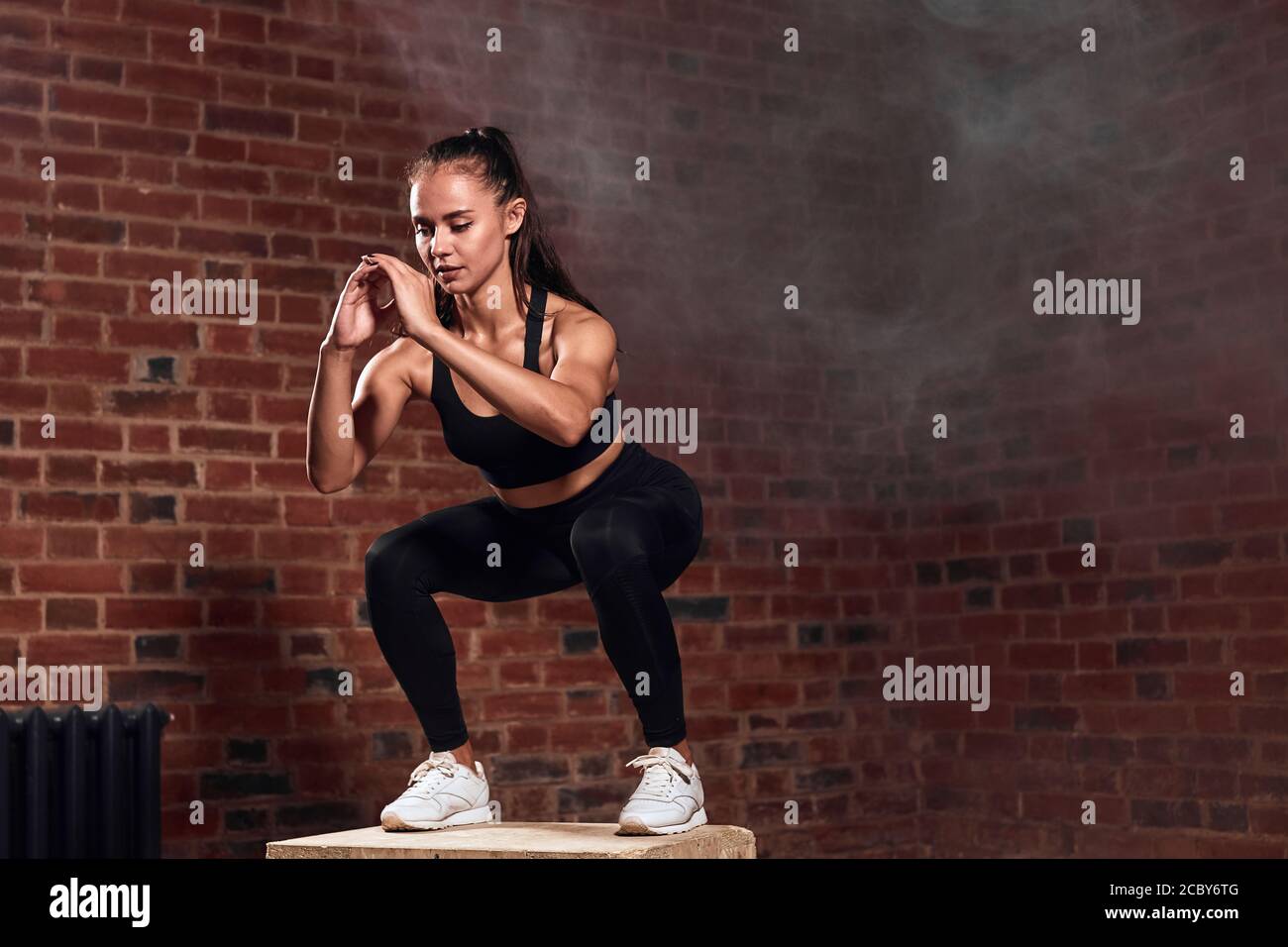 Slim sport woman in sportswear jumping on fit box and do squats