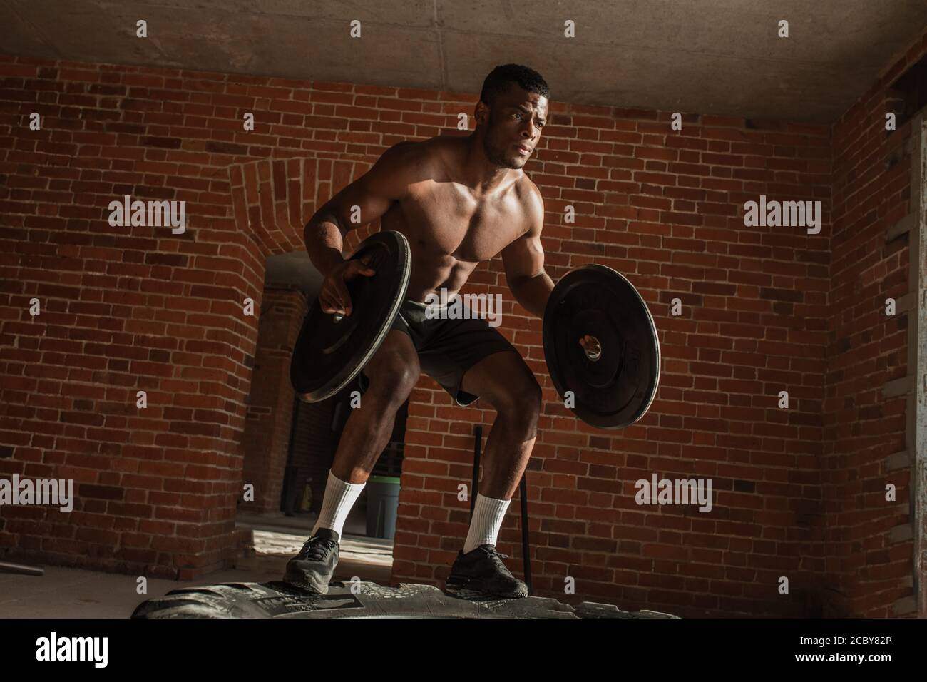 Powerful strong african fighter boxer practicing Weighted Jumps with  barbell plates on and over big lying truck tire in crossfit studio against  brick Stock Photo - Alamy
