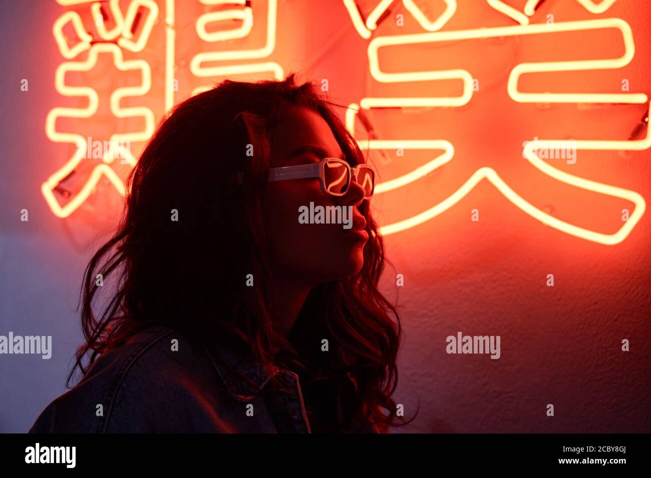 African woman wears trendy glasses profile in red neon backlight in night club. Stock Photo