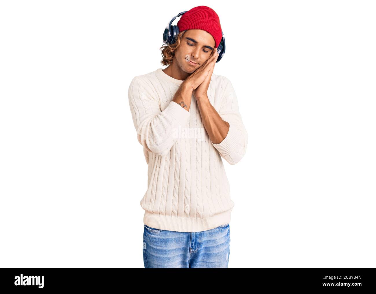 Young hispanic man listening to music using headphones sleeping tired dreaming and posing with hands together while smiling with closed eyes. Stock Photo