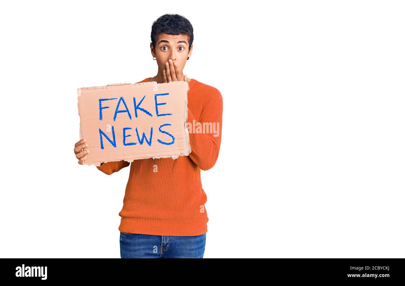 Young african amercian man holding fake news banner covering mouth with ...