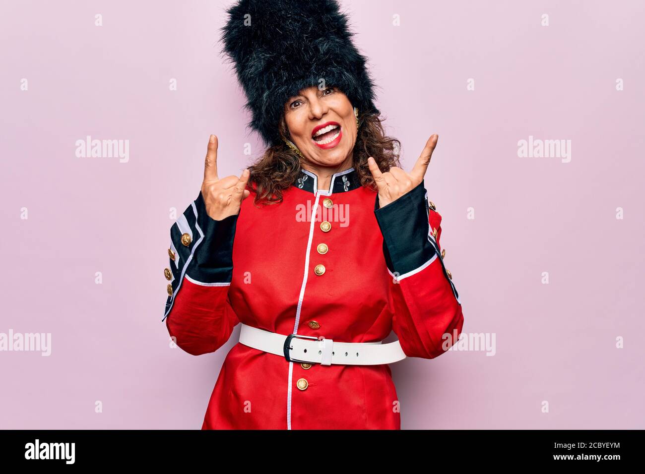 Middle age beautiful wales guard woman wearing traditional uniform over pink background shouting with crazy expression doing rock symbol with hands up Stock Photo