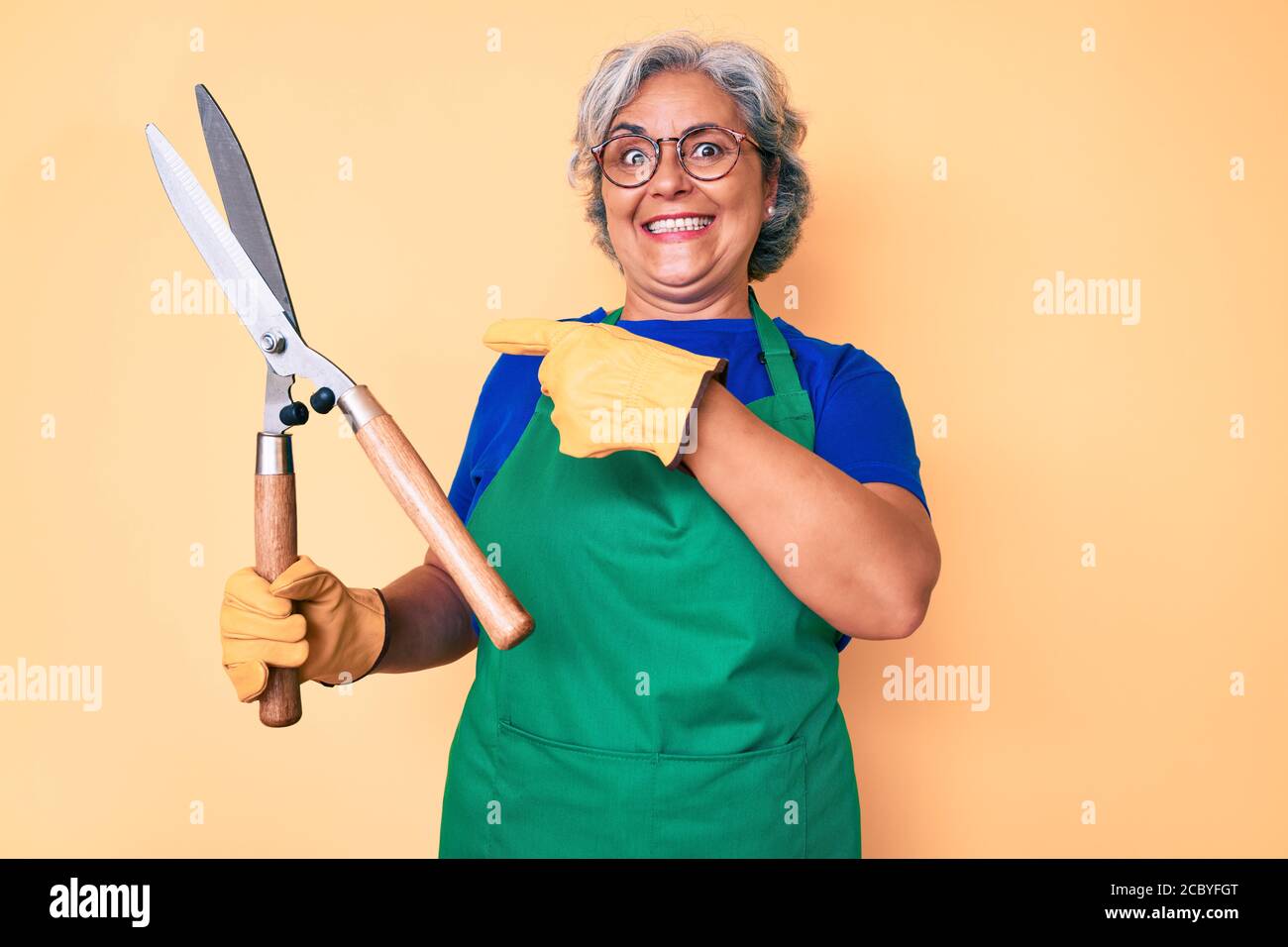 Senior hispanic woman wearing gardener apron and gloves holding shears ...
