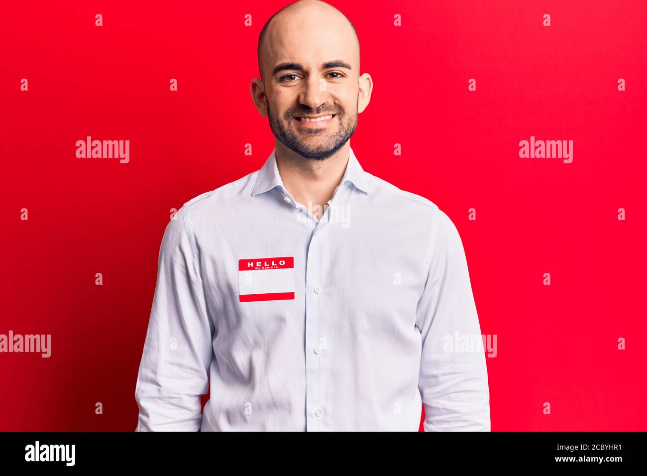 Young handsome bald man wearing hello my name is sticker looking ...