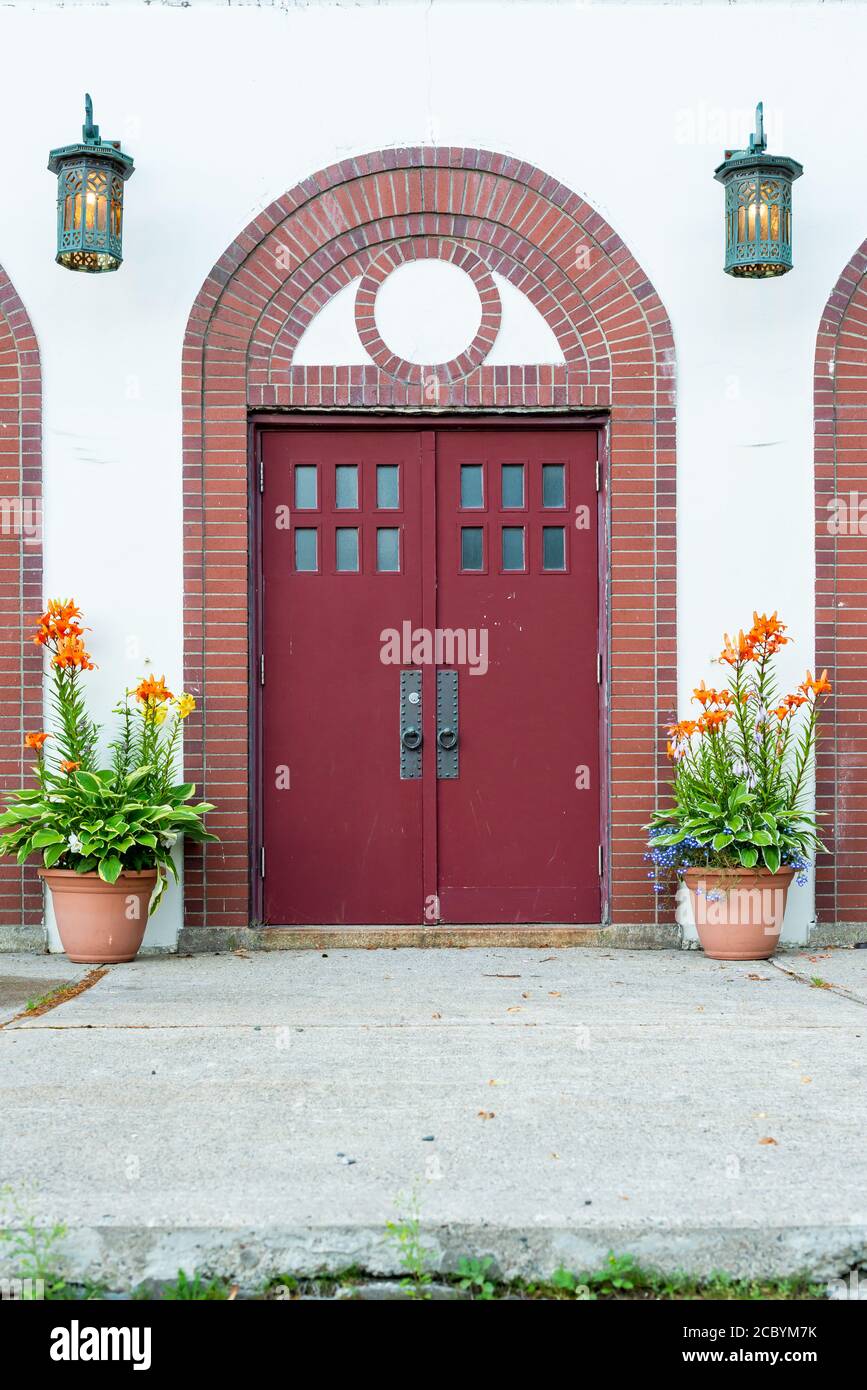Two tall red doors with small square windows on the top of the wooden
